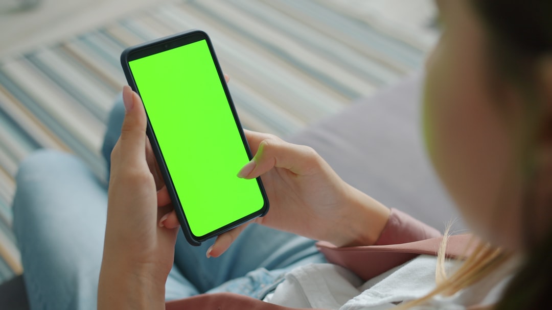 Close-up of woman using smartphone with blank chroma key screen in house sitting alone swiping enjoying social media online. People and internet concept.